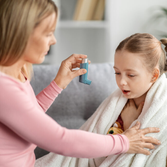Preventing Attack. Caring mother giving asthma inhaler to sick child at home